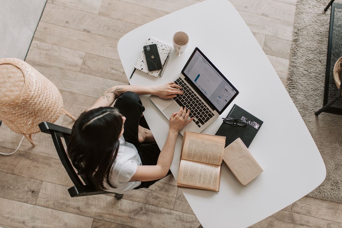 Adult working at a white desk with an open laptop, books, and a mug