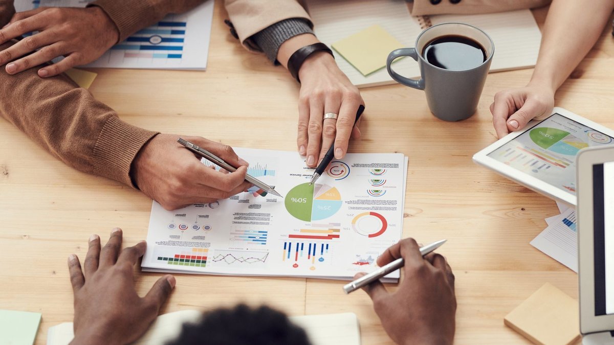 Overhead view of colleagues pointing at colourful charts on a table beside a tablet